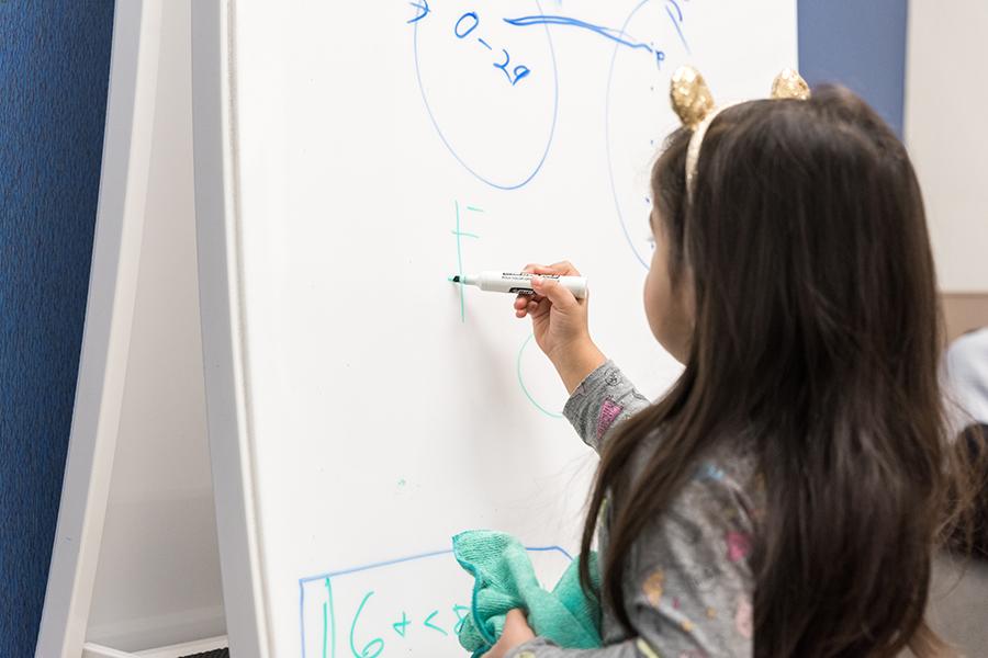 A little girl writing on a dry erase board.