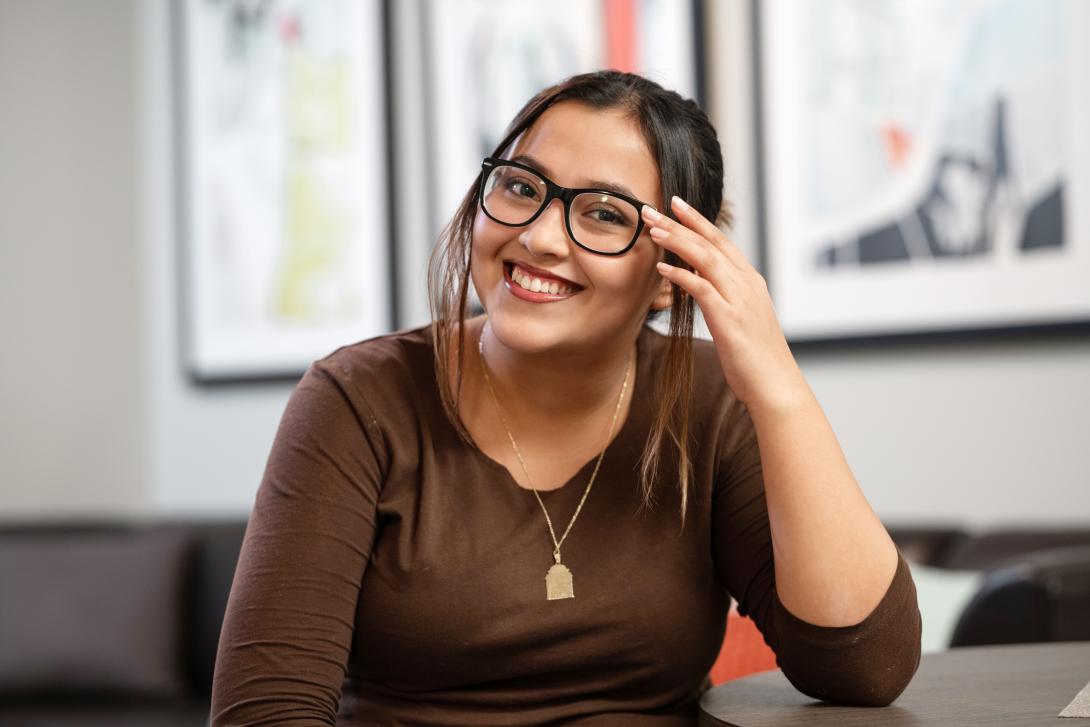 A female NEIU student wearing glasses sits behind a table