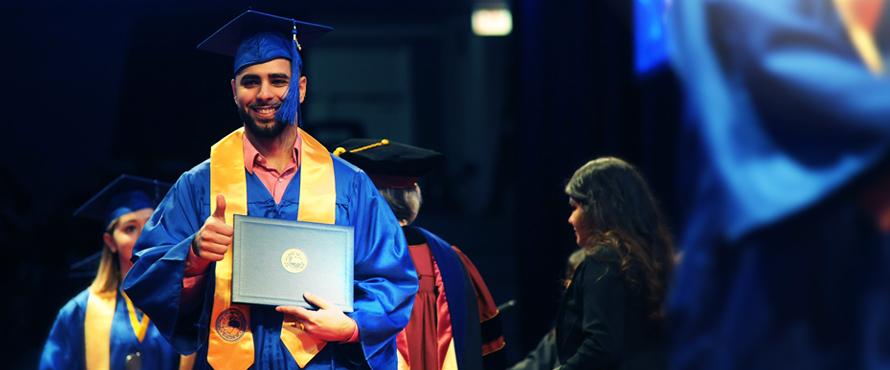 At Commencement, graduate walking the stage with diploma cover in hand.