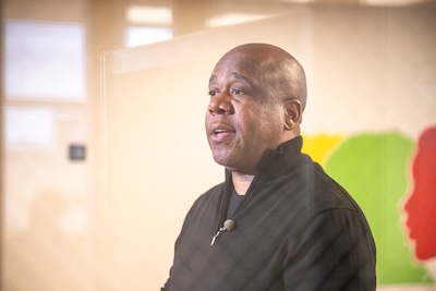 A photo of Torrence Price wearing a black shirt, talking in the library at Northeastern Illinois University's Jacob H. Carruthers Center for Inner City Studies.