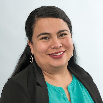 A headshot photo of Wendy Gonzales, smiling, wearing a green blouse and black blazer against a light gray background.