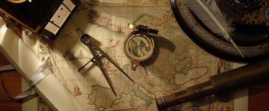 A compass, quill and other mapmaking tools lie atop an old map of the world