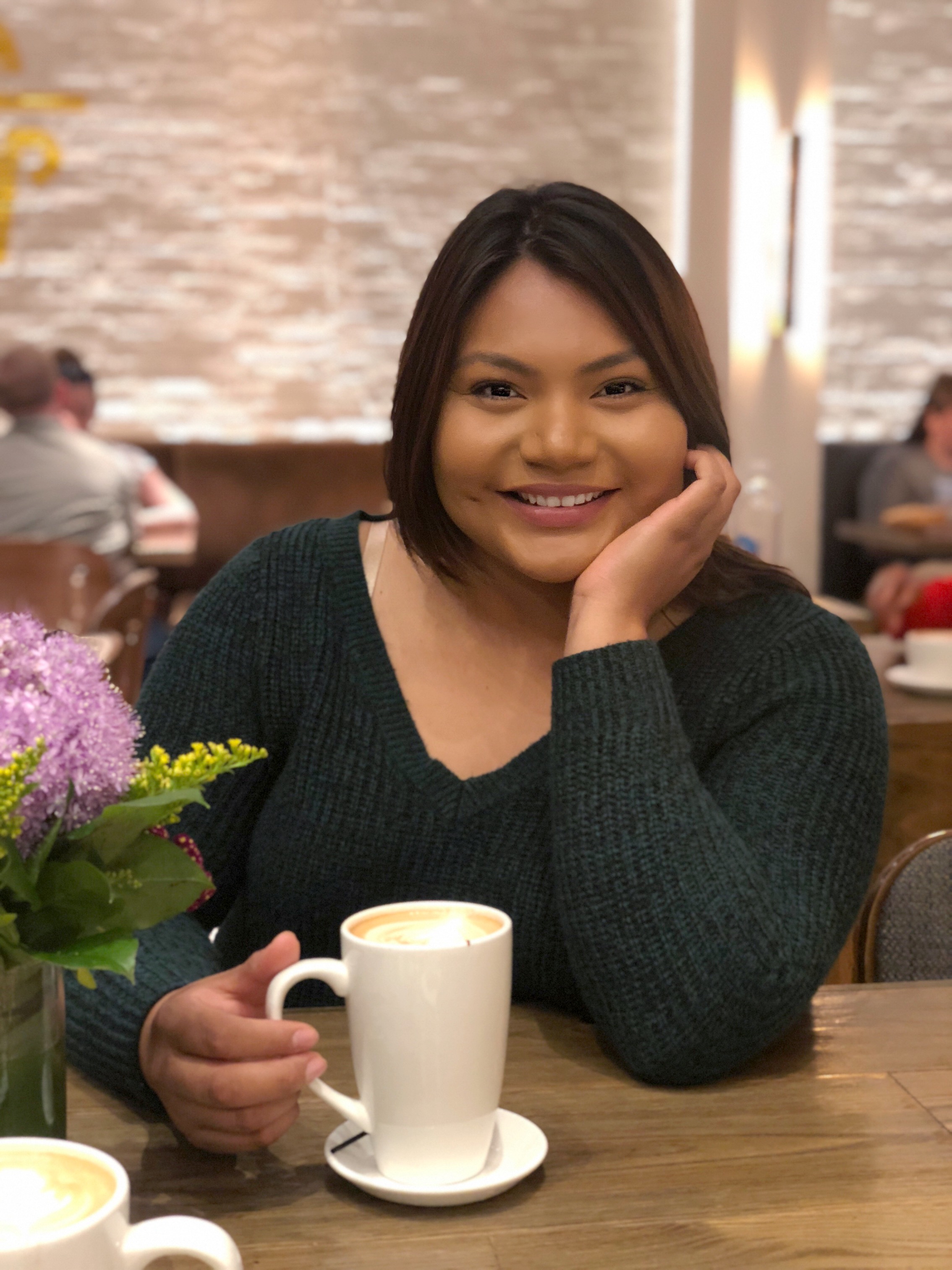Cecelia Hernandez smiles into the camera while holding a cup of coffee.