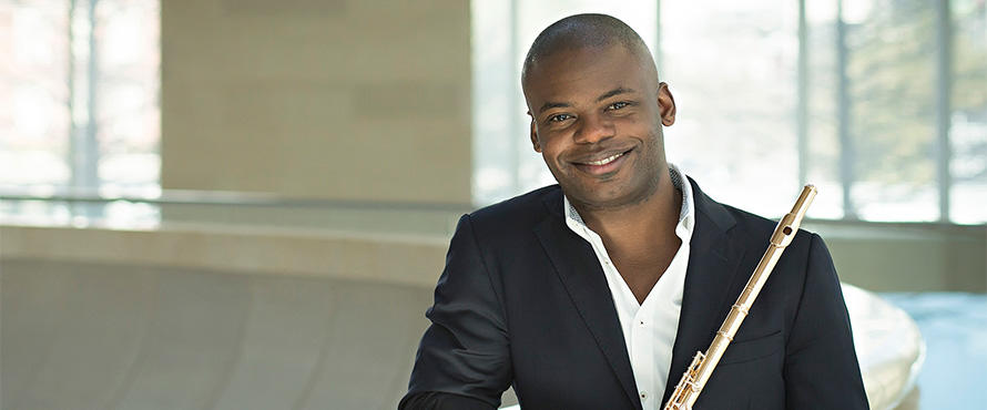 Flutist Demarre McGill holds a flute and poses indoors in front of windows