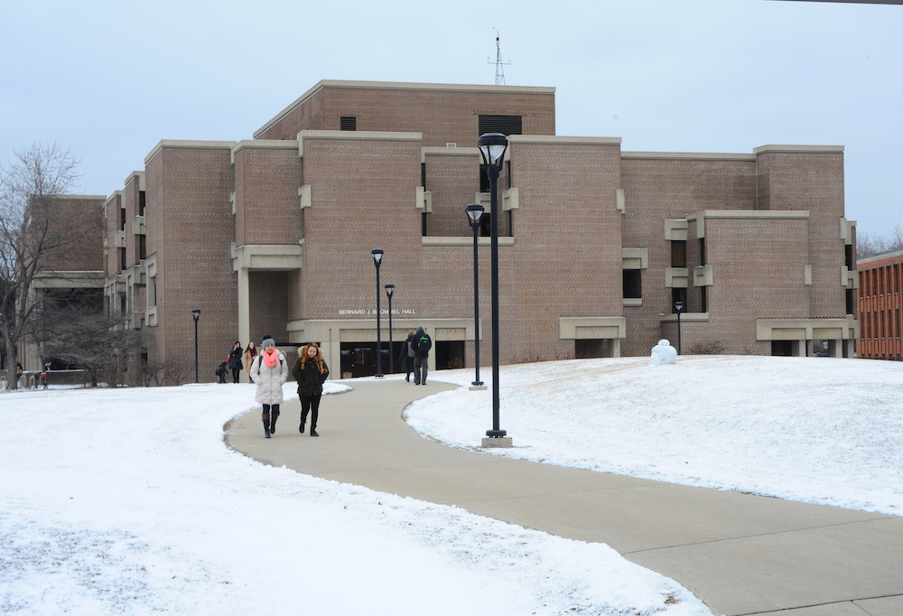 The western exterior of Bernard Brommel Hall in winter with people walking on the paths of the University Commons in the foreground