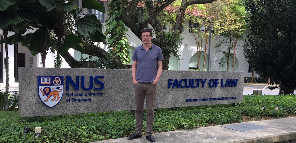 Assistant Professor of Business Law Richard Kilpatrick stands outdoors in front of National University of Singapore signage