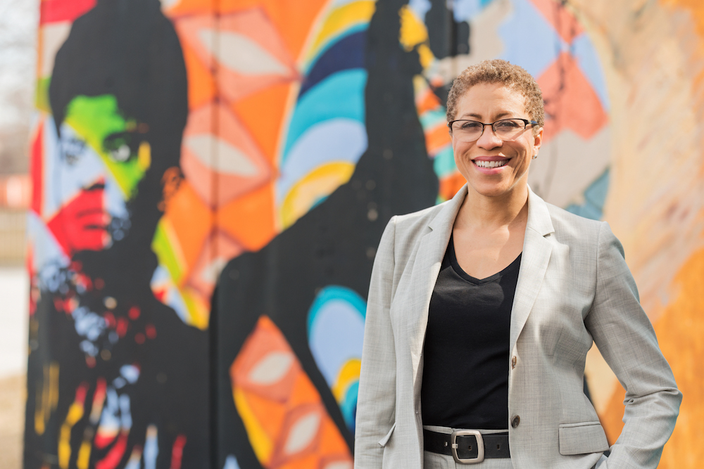 Carruthers Center Director Andrea Evans stands in front of a colorful mural 