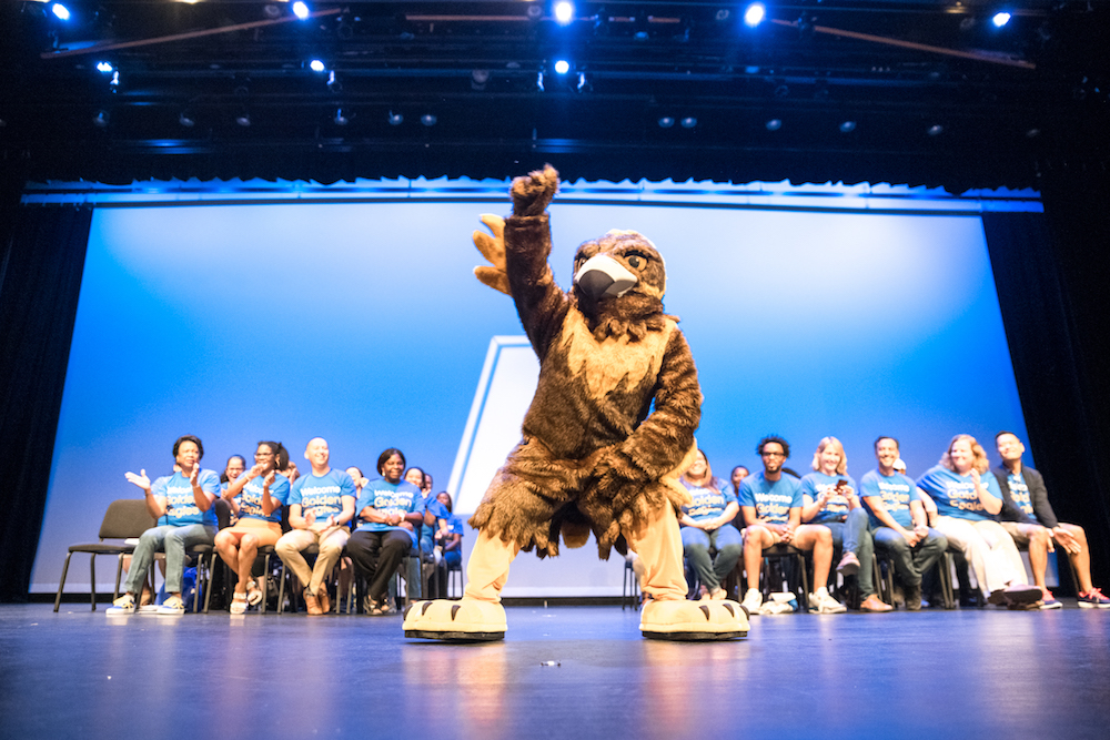 NEIU mascot Goldie the Golden Eagle raising a wing on the Auditorium stage