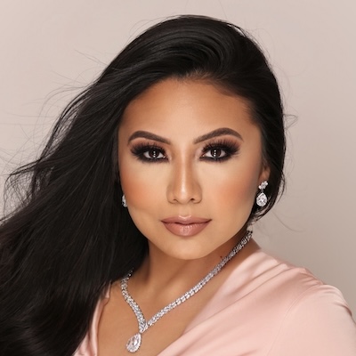 A headshot photo of Alicia Manzanares wearing a light pink blouse, silver necklace and earrings against a light pink background.