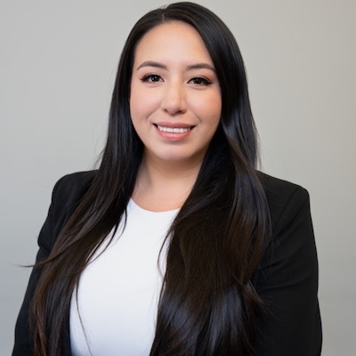 A headshot photo of Melanny Buitron Loor wearing a black blazer and white blouse against a gray background.