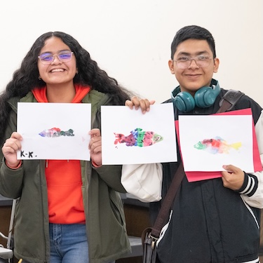 A photo of two young students at the 2024 Chicago River Student Congress holding up their paintings of fish. 