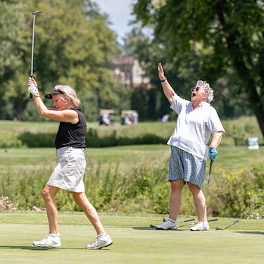 A photo of Chuck Kane's daughters, Mary and Liz Kane, playing a round of golf during the Chuck Kane Golf Outing. 