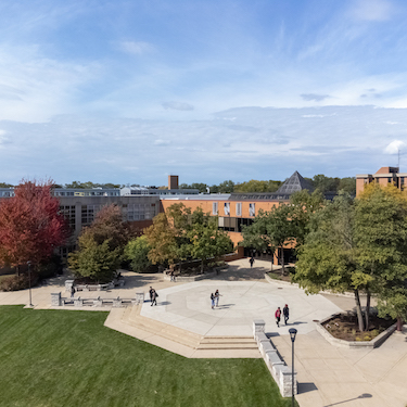 An aerial photo of NEIU's Main Campus overlooking the University Commons and Student Union. A few people are walking on the University Commons on a sunny day with partly cloudy skies.