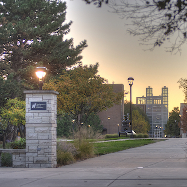 A photo of the entrance to NEIU's Main Campus from St. Louis Ave. with a view of the path runs across the University Commons to the Parking Facility, visible in the background.