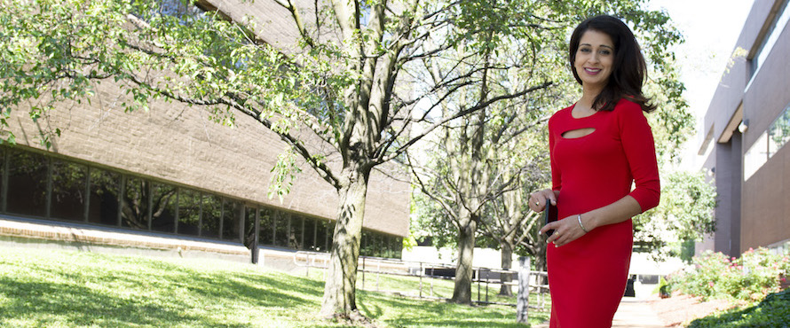 PJ Randhawa  wearing a red dress stand outdoors with trees in the background