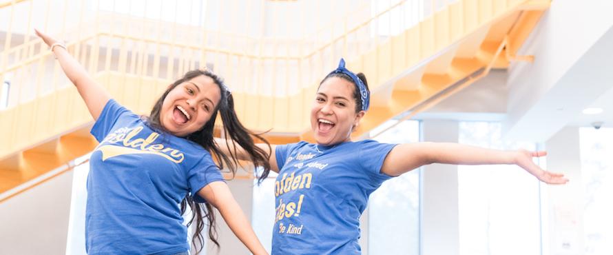 A photo of two Northeastern students smiling with arms outstretched in NEIU t-shirts 