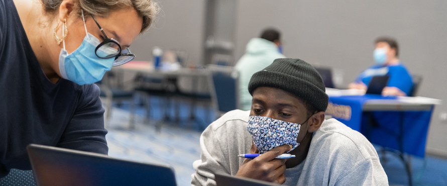 Photo of a Northeastern academic advisor in a face mask meeting with a student with a face mask during a Fall 2021 registration event.