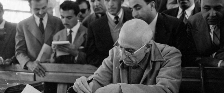 Mohammad Mossadegh seated at a table writing