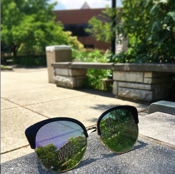 A building is reflected in a pair of sunglasses that sit on a table.